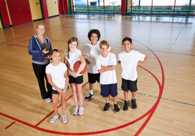 Multi-ethnic elementary or middle school students in school gym with coach playing basketball.